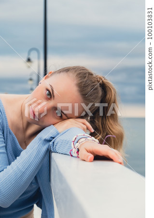 Young woman standing on wooden pier blurred beachside background. Attractive female enjoying the sea shore travel and active lifestyle concept. Springtime. Wellness wellbeing mental health inner peace 100103831