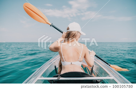 Woman in kayak back view. Happy young woman with long hair floating in transparent kayak on the crystal clear sea. Summer holiday vacation and cheerful female people relaxing having fun on the boat Woman in kayak back view. Happy young woman with long hair floating in transparent kayak on the crystal clear sea. Summer holiday vacation and cheerful female people relaxing having fun on the boat 100105780
