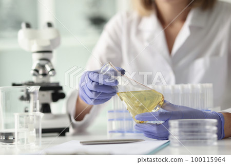 Scientist sits in research laboratory and holds flask in her hand. 100115964