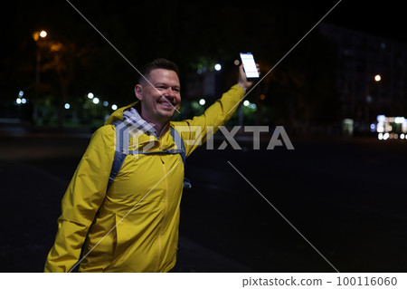 Smiling man holds cellphone in his hand and welcoming friend in evening street. Smiling man holds cellphone in his hand and welcoming friend in evening street. 100116060
