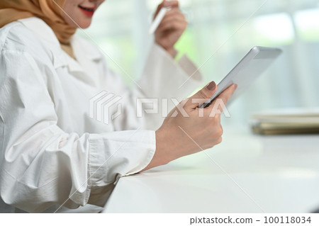 Cropped shot of smiling young muslim woman using digital tablet, enjoying freelance work in home office Cropped shot of smiling young muslim woman using digital tablet, enjoying freelance work in home office 100118034