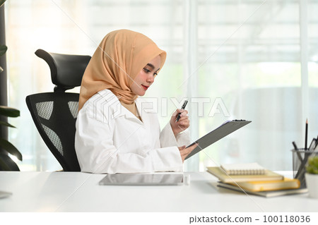 Portrait of muslim businesswoman sitting in her office and reading information on document Portrait of muslim businesswoman sitting in her office and reading information on document 100118036