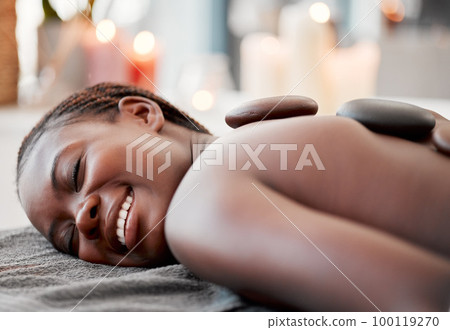 Hot stone massage, black woman at spa with smile on face, holistic healing with physical therapy and back skin detox. Happy, content and zen with wellness at luxury resort, rocks and relax with glow 100119270