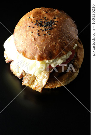 A bird's-eye view of a BLT burger with bacon, lettuce, and tomato with tartar sauce protruding in a black background 100120230