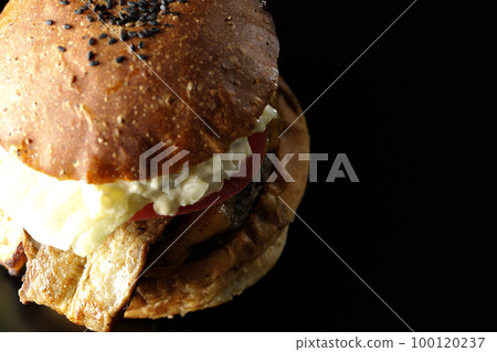 A bird's-eye view of a BLT burger with bacon, lettuce, and tomato with tartar sauce protruding in a black background 100120237