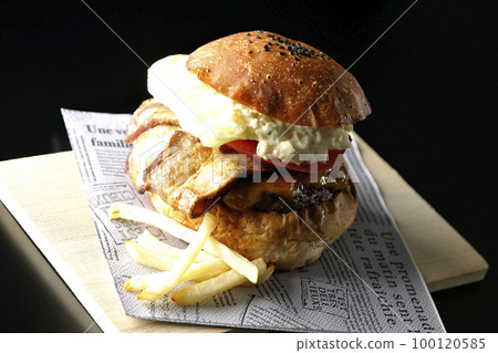 BLT burger and fries with bacon, lettuce and tomato with tartar sauce protruding in black background 100120585