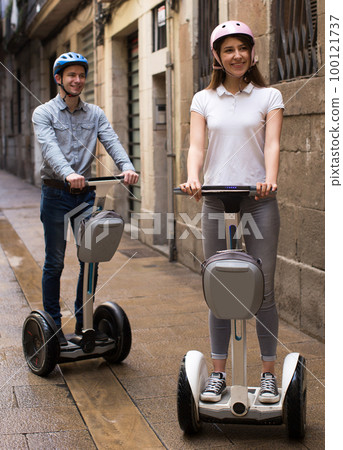 young couple guy and girl walking on segway in streets of european city 100121737