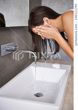 Morning routine. A cropped shot of a young woman washing her face in her bathroom. Morning routine. A cropped shot of a young woman washing her face in her bathroom. 100121795