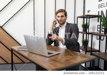 busy lawyer talking on the phone in the office with a client and looking at a laptop 100122251