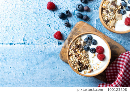 Yogurt with berries and muesli for breakfast in bowl on blue background. Top view. Copy space Yogurt with berries and muesli for breakfast in bowl on blue background. Top view. Copy space 100123808