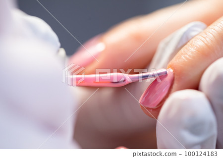 The manicurist paints the client's nails using a brush. 100124183