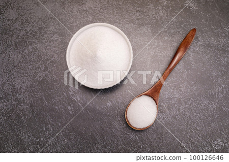 Organic sweetener Erythritol, produced by fermentation from corn, called dextrose in ceramic bowl, wooden spoon on granite background, table. Sugar substitute. Horizontal plane, top view, copy space 100126646