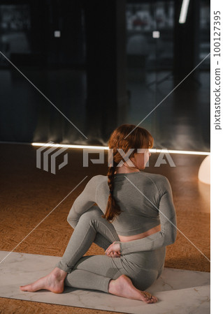 A girl in a gray sports uniform does yoga on a mat in the gym 100127395