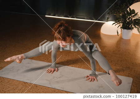 A girl in a gray sports uniform does yoga on a mat in the gym 100127419