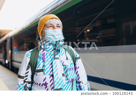 Old woman in yellow hat waiting on station platform with backpack on train background. Railroad transport concept, Traveler 100128143