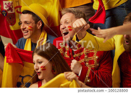 Live game. People, football, soccer fans emotionally watching match, cheering up favourite team. Fans wearing colorful scarves and flags Live game. People, football, soccer fans emotionally watching match, cheering up favourite team. Fans wearing colorful scarves and flags 100128800