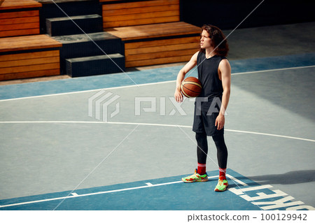 Sports guy on the basketball court, a guy with long hair trains with the ball on the basketball court, streetball. 100129942