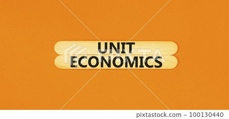 Unit economics symbol. Concept words Unit economics on wooden stick. Beautiful orange table orange background. Business and unit economics concept. Copy space. 100130440