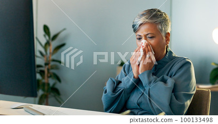 Business woman blowing her nose in the office while working on a report, document or research. Sick, professional and ill senior employee planning a corporate project or proposal in modern workplace. Business woman blowing her nose in the office while working on a report, document or research. Sick, professional and ill senior employee planning a corporate project or proposal in modern workplace. 100133498
