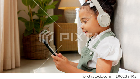 Tablet game, headphones and relax child gaming, having fun or play online games on mobile device or digital tech app. Kid entertainment, youth lifestyle and young gamer girl playing on ui touchscreen 100135402