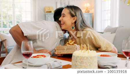 Interracial couple, gift and celebrate birthday being happy, kiss and smile in home at table with cake. Love, man and woman being content, romantic and present being cheerful celebration together. Interracial couple, gift and celebrate birthday being happy, kiss and smile in home at table with cake. Love, man and woman being content, romantic and present being cheerful celebration together. 100135916