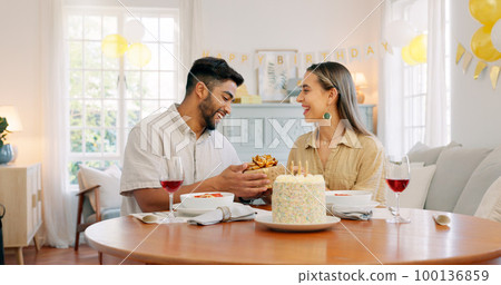 Interracial, couple and celebrate for birthday with gift, being happy and relax together at party. Romance, man and woman with present, bonding and smile in home in living room for hug and embrace. Interracial, couple and celebrate for birthday with gift, being happy and relax together at party. Romance, man and woman with present, bonding and smile in home in living room for hug and embrace. 100136859