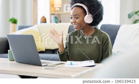 Woman talking on videocall using laptop and headphones while waving hello to friends online. Student making notes while communicating and learning new language during online course or private lesson Woman talking on videocall using laptop and headphones while waving hello to friends online. Student making notes while communicating and learning new language during online course or private lesson 100139423