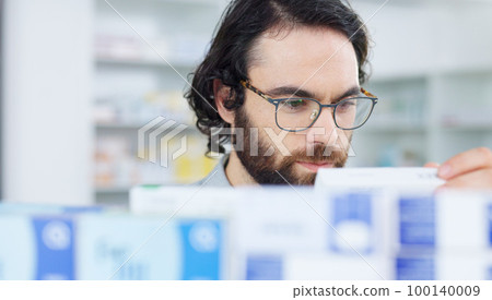 Man with glasses choosing medication on a shelf in a pharmacy. Customer with glasses browsing in aisle in a drugstore and finding what he needs before heading to the checkout with his vitamins 100140009