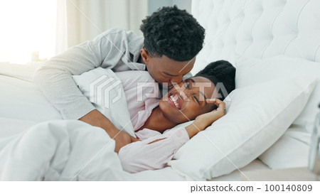 Relax, couple and love in bedroom kiss, rest and comfort in happy relationship together at home. Man and woman lying in bed relaxing, talk and smile in comfortable house and morning happiness 100140809