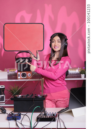 Asian performer holding red speech bubble advertising text messages cardboard in studio over pink background. Musician playing sounds to produce melody at professional mixer console Asian performer holding red speech bubble advertising text messages cardboard in studio over pink background. Musician playing sounds to produce melody at professional mixer console 100141233