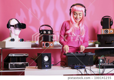 Artist with headphones playing electronic song at professional turntables, performing techno music in front of fans. Musician with pink hair doing performance at nightclub with audio equipment Artist with headphones playing electronic song at professional turntables, performing techno music in front of fans. Musician with pink hair doing performance at nightclub with audio equipment 100141235