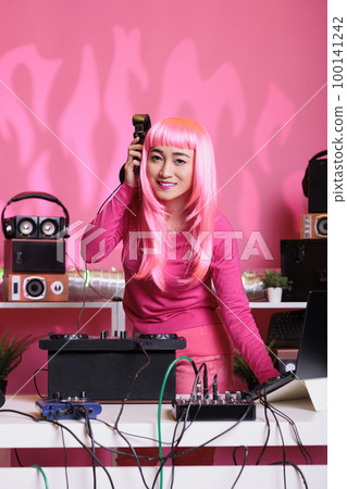 Asian performer dancing while playing techno music at professional turntables while having fun with fans in club during night time. Dj artist performing song using professional audio equipment Asian performer dancing while playing techno music at professional turntables while having fun with fans in club during night time. Dj artist performing song using professional audio equipment 100141242