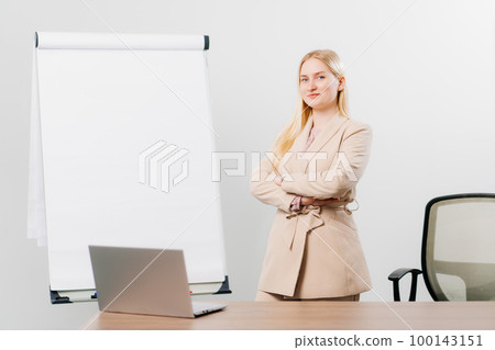 a blonde in a suit in an office with a board for meetings, desktop and laptop 100143151