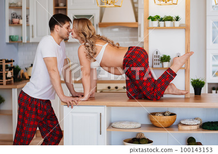 a pregnant woman and a man in pajamas flirt in the kitchen 100143153