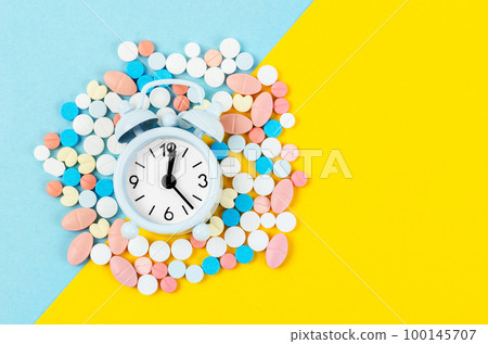 The pills and alarm clock on the blue and yellow color background The pills and alarm clock on the blue and yellow color background 100145707
