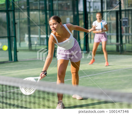 Young woman padel tennis player trains on the outdoor court Young woman padel tennis player trains on the outdoor court 100147346