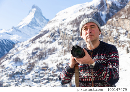 Interested man photographer capturing mountain views hiking in Swiss Alps 100147479