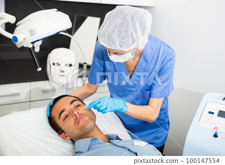 Professional beautician performing face carboxytherapy to male client 100147554