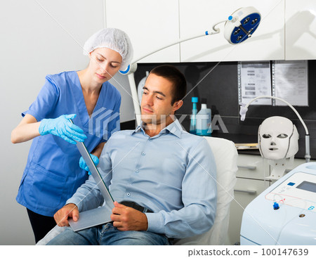 Female cosmetician explaining client hardware facial procedure Female cosmetician explaining client hardware facial procedure 100147639