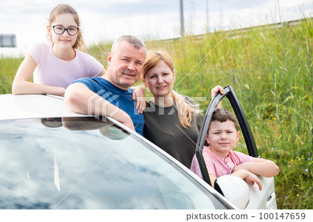 Happy family of four posing next to purchased car 100147659