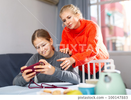 Daughter plays on smartphone while mother tries to talk to her Daughter plays on smartphone while mother tries to talk to her 100147883