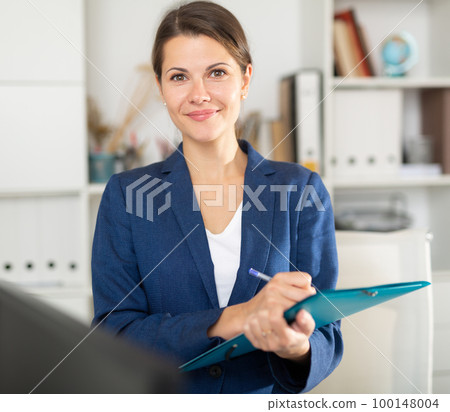 Smiling female business assistant noting tasks on clipboard 100148004