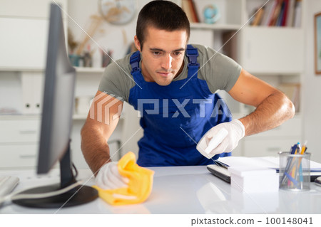 Male cleaner wipes table with rag in office 100148041