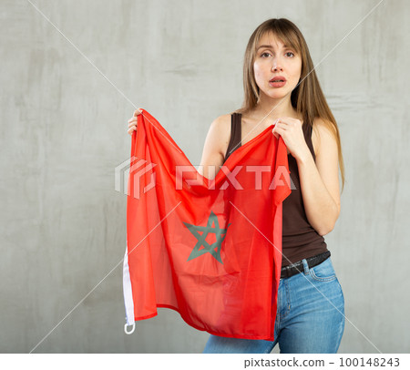 Sad young woman holding flag of Morocco against unicoloured background Sad young woman holding flag of Morocco against unicoloured background 100148243