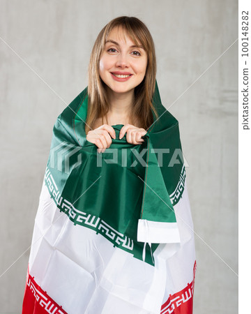 Happy young woman holding flag of Iran against unicoloured background Happy young woman holding flag of Iran against unicoloured background 100148282