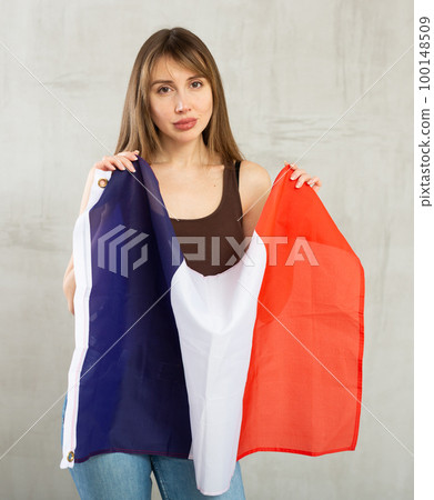 Sad young woman holding flag of France against unicoloured background 100148509