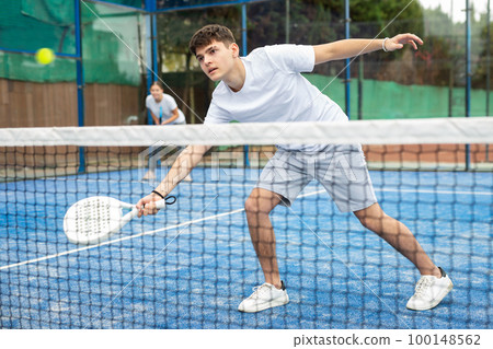 Sporty young guy playing padel on open court Sporty young guy playing padel on open court 100148562