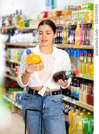 Young girl reading labels on bottles of juices in supermarket 100148889