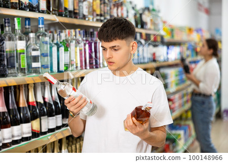 man chooses between vodka and cognac in supermarket man chooses between vodka and cognac in supermarket 100148966