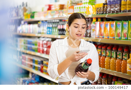 Young woman searching information about juices on internet in supermarket Young woman searching information about juices on internet in supermarket 100149417